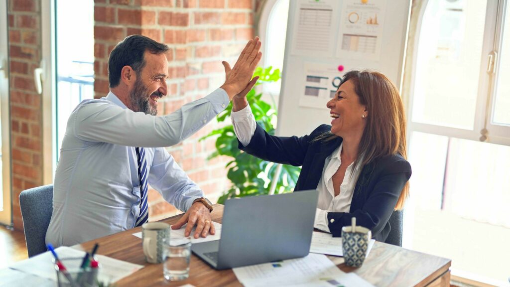 Geschäftspartner geben sich im Büro ein High-Five und lachen zufrieden über ihren Erfolg